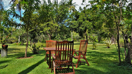 The garden lawn has a wooden table and chairs. Tropical vegetation grows around. Relaxing on a sunny summer day. Maldives