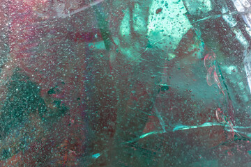 Crystal glass for the backdrop. Colors - shades of green, red. Frozen air bubbles, cracks and scratches. Ice piece concept. Selective focus.