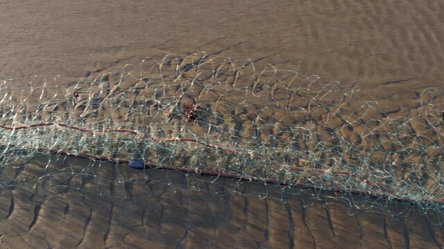 Empty industrial fishing net lays on the beach sand. 