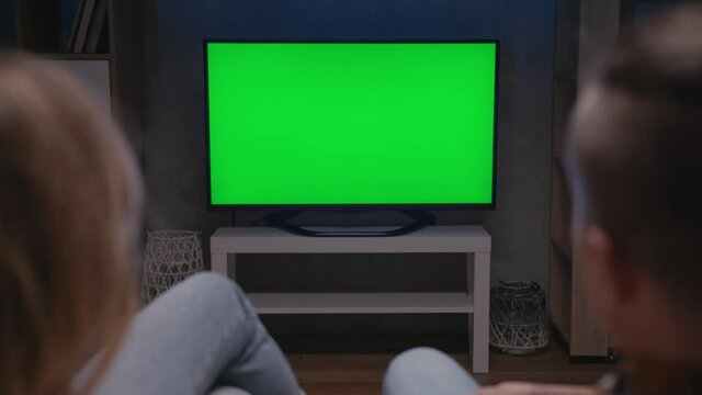 Family Couple Watches Green Screen TV Mockup Sitting on Couch in Living Room Together. Rear View on Casual People who Watching TV Green Screen in Domestic Cinema. Looking TV Show or News in Home Rest