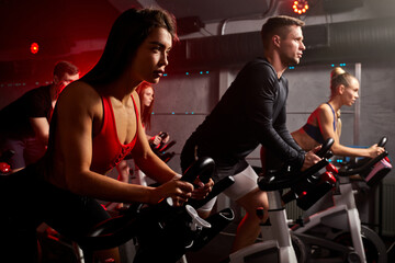men and women biking in gym, exercising legs doing cardio workout cycling bikes, spinning in health...
