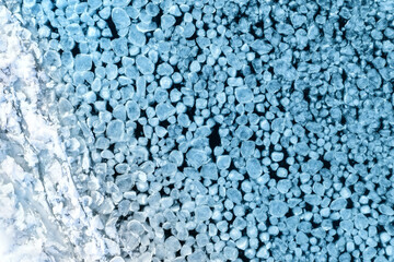 Abstract texture of broken white ice in blue water near a snowy shore. View of the ice from a drone. Background from the frozen surface of a clean lake or river