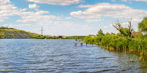 Bank of sunny summer lake with green reed thickets and several wooden piers for fishing and swimming