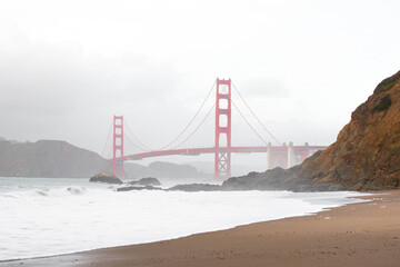 Famous Golden Gate Bridge seen from scenic Baker Beach in foggy day.