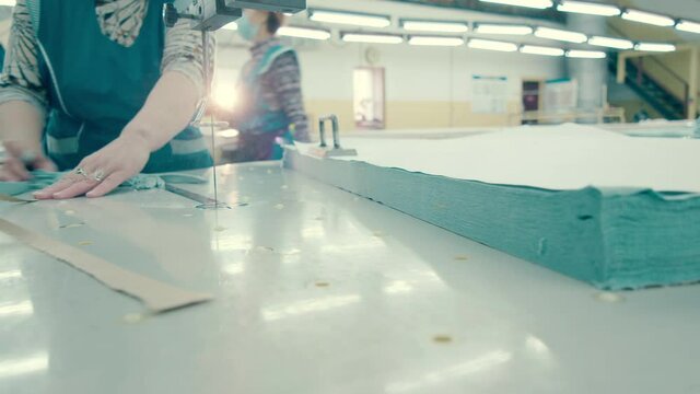 Textile worker is cutting off edges of the clothing material