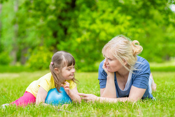 Mother talks with little girl with syndrome down in a summer park