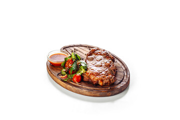 Juicy appetizing grilled steak served with a salad of tomato and green leaves and with red sauce. Food served on a wooden board. Isolated