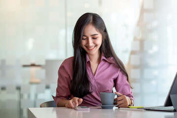 Beautiful asian woman happy to drink coffee and play on the phone at desk office.