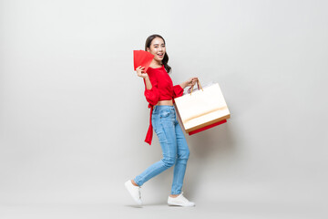 Happy Asian woman holding shopping bags and red envelopes or Ang Pao isolated in light gray studio background for Chinese new year sale concept