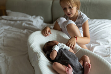 Little sister and her newborn brother. Toddler kid meeting new sibling. Cute girl and new born baby boy relax in a home bedroom. Family with two children at home. Love, trust and tenderness concept