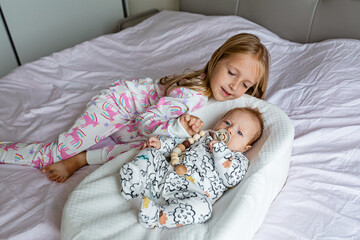 Little sister and her baby brother. Toddler kid playing with new sibling. Girl and baby 2-3 months old relax in a home bedroom. Family with two children at home. Love, trust and tenderness concept
