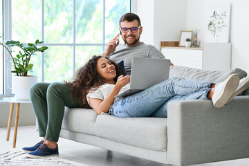 Young couple with gadgets relaxing on sofa at home