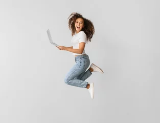 Fotobehang Young woman with laptop jumping on light background © Pixel-Shot