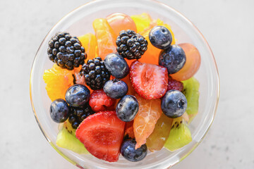 Glass with fruit salad on light background
