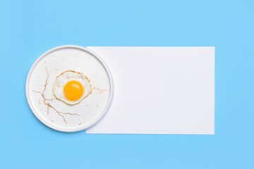 Plate with tasty fried egg and blank sheet of paper on color background