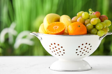 Colander with different fruits on table outdoors