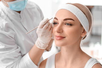 Young woman undergoing eyebrow correction procedure in beauty salon