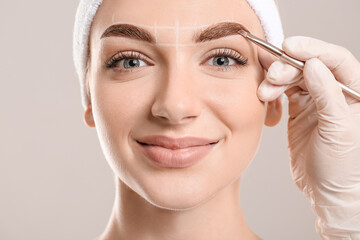 Young woman undergoing eyebrow correction procedure on grey background