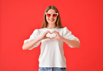 Young woman making heart with her hands on color background