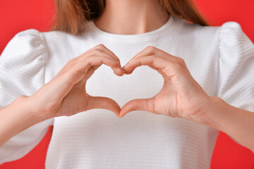 Young woman making heart with her hands on color background, closeup