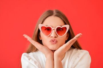 Beautiful young woman in stylish heart-shaped sunglasses on color background