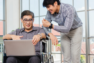 Fototapeta na wymiar Asian senior disabled businessman in a wheelchair with laptop computer discuss together with team in office. Old father man sitting wheelchair and his son talking video calls conference on laptop