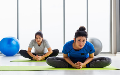 Fototapeta na wymiar Two Asian women sporty attractive people practicing yoga lesson together, working out at the fitness GYM, Young and senior female exercising do yoga in yoga classes, sport healthy lifestyle