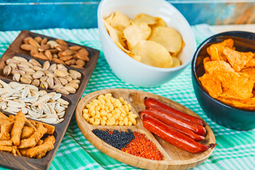 Assorted snacks, bowl of chips and a plate of sausages on a blue table
