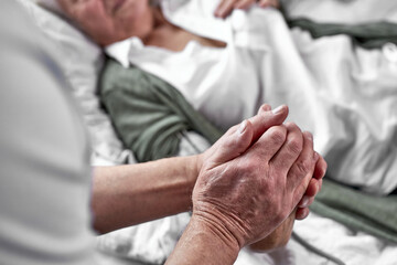 elderly man crying and mourning the loss of his wife, sitting by her side. focus on hands....