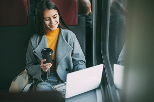 Freelance girl drinks coffee and sits on the train with a working laptop. Modern technologies and networks