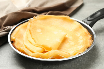 Pan with thin pancakes and kitchen towel on gray background