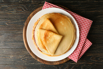 Board with thin pancakes on wooden background