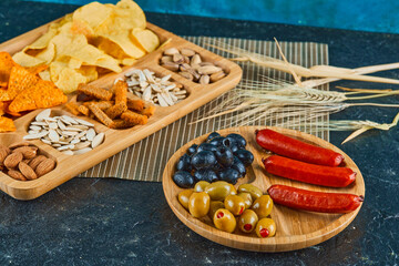 Assorted snacks, a plate of sausages and olives on dark table