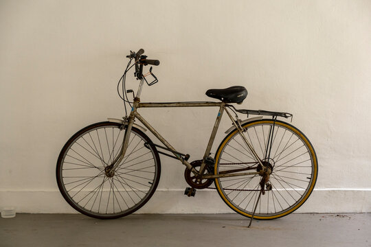 Rusty and dirty vintage bicycle by a white painted wall. Stock Photo.