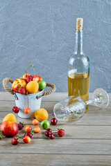 Bucket of fresh summer fruits, bottle of white wine and empty glass on wooden table