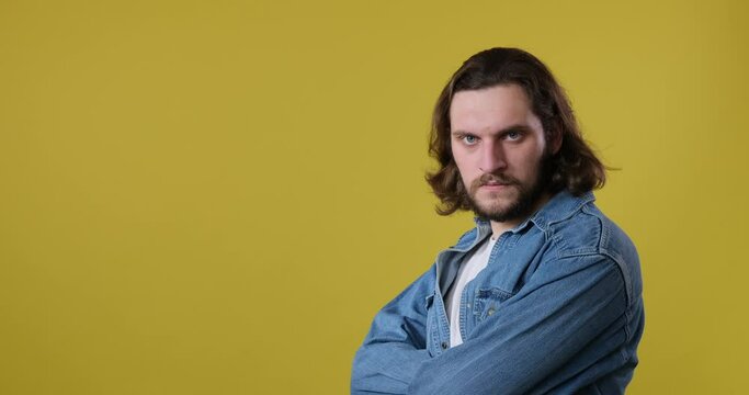 Serious man in denim jacket with arms crossed over yellow background