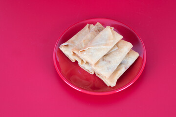 A plate of fried spring rolls on a red background