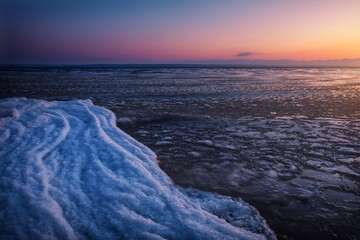 Natural Winter landscape on seashore during sunset. Ice and sunset sky.