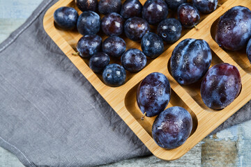 Garden plums on wooden platter with gray tablecloth