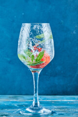 A glass of juice with strawberries and mint inside on blue background