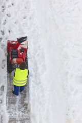 Worker cleaning snow on the sidewalk with a snowblower. Wintertime