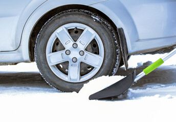 Cleaning car wheels from snow with a shovel. Snow removal tool. Selective focus.