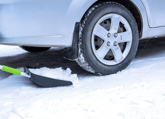 Removing snow with a hand shovel under the car. Selective focus.