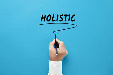 Businessman hand writing the business buzzword holistic on blue background. Holistic approach in business