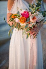 Bride holds wedding bouquet near sea