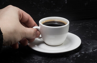 a woman takes a white cup with black aromatic coffee in her hands to enjoy its taste