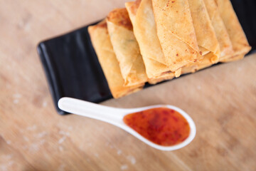 Look down at a plate of fried spring rolls and a spoon of dip