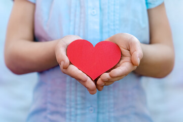 Girl holding a red heart in her hands, close-up. Female hands holding a heart in their hands, Valentine's Day, love, romantic blue background. Give a valentine. Declaration of love