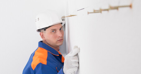 the wall with the line on which the screws are twisted, the worker checks the correctness of the...