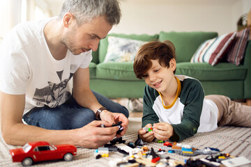 Handsome young caucasian father or male baby sitter playing with cute boy kid by multicolored building bricks on floor in living room at home. Educational games concept. Activity with children